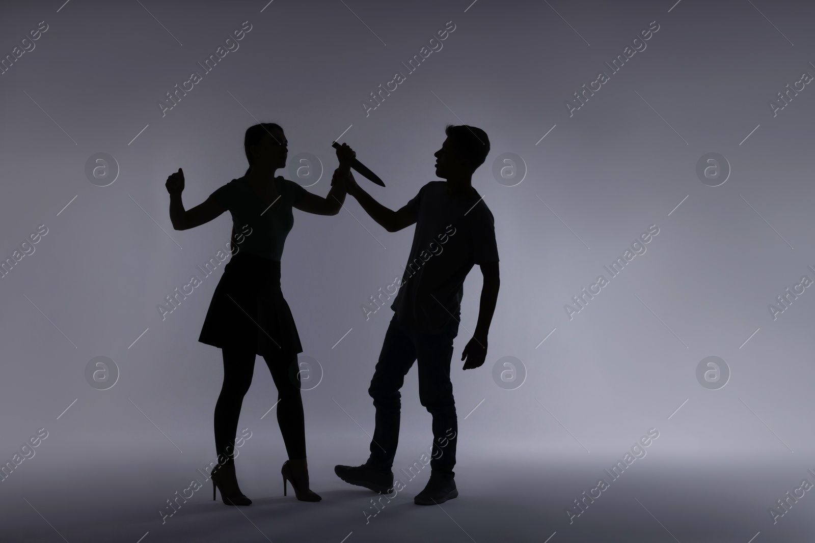 Photo of Domestic violence. Silhouette of woman with knife threatening her husband on grey background