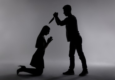 Photo of Domestic violence. Silhouette of man with knife threatening his wife on grey background