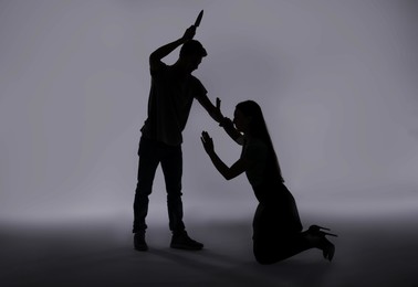 Photo of Domestic violence. Silhouette of man with knife threatening his wife on grey background