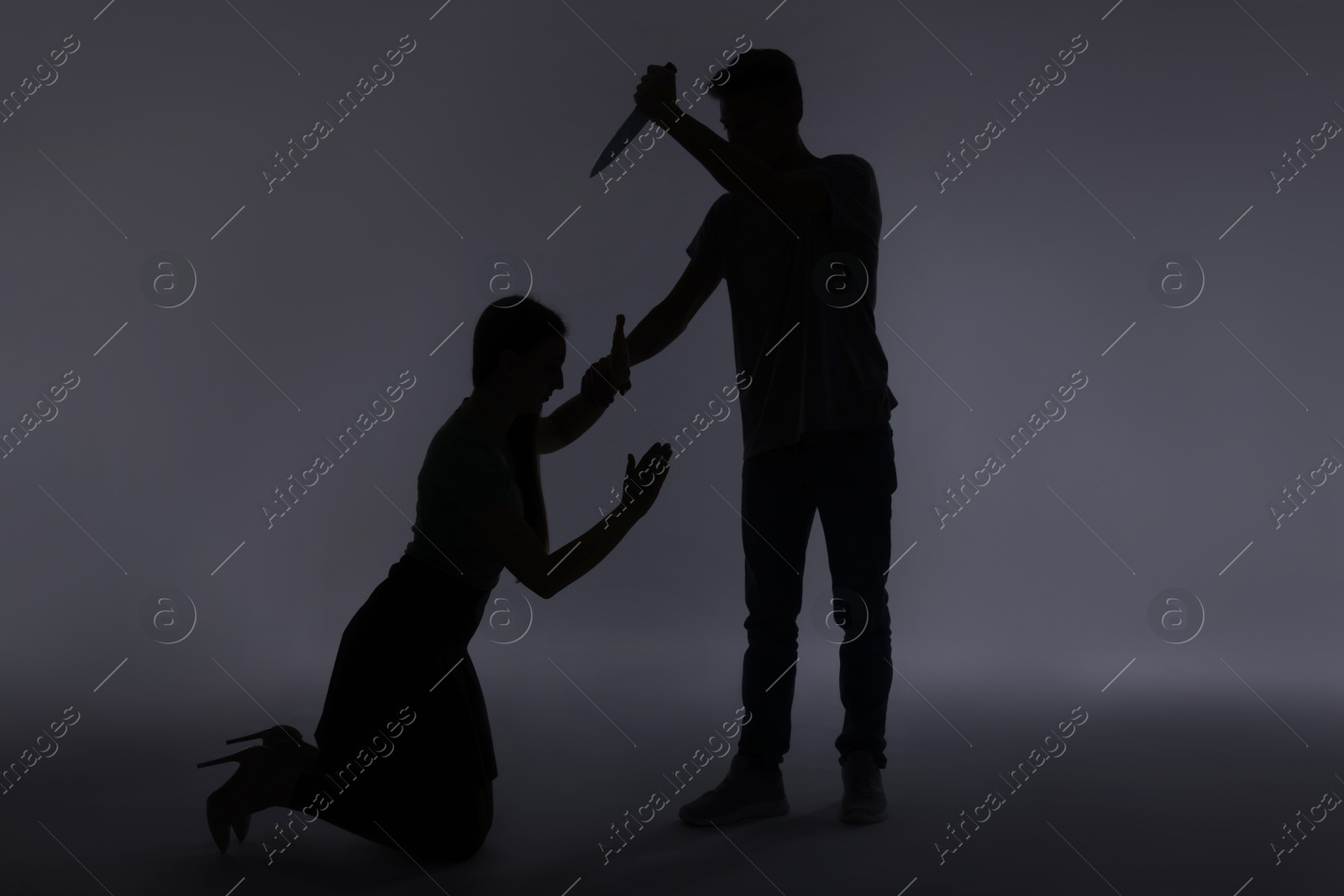 Photo of Domestic violence. Silhouette of man with knife threatening his wife on grey background