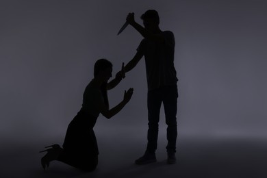 Photo of Domestic violence. Silhouette of man with knife threatening his wife on grey background