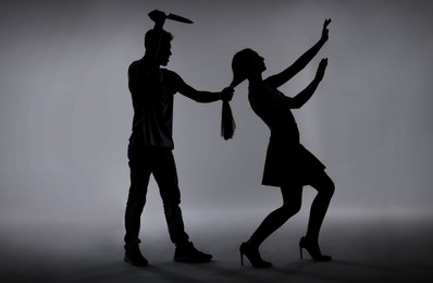 Photo of Domestic violence. Silhouette of man with knife trying to kill his wife on grey background