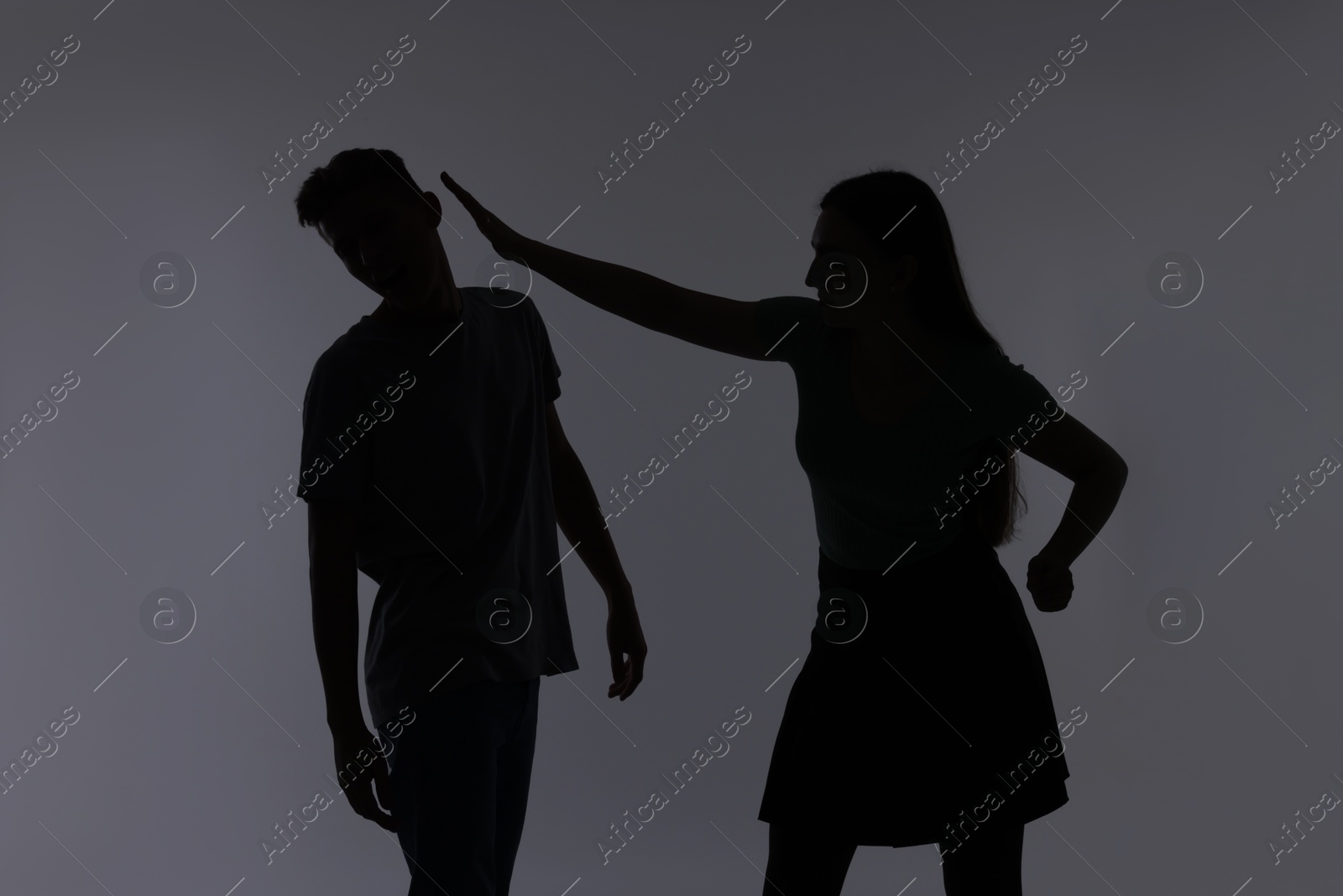 Photo of Domestic violence. Silhouette of woman punching her husband on grey background