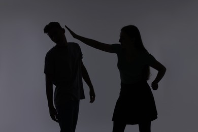 Photo of Domestic violence. Silhouette of woman punching her husband on grey background