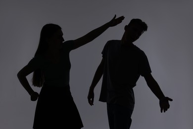 Photo of Domestic violence. Silhouette of woman punching her husband on grey background