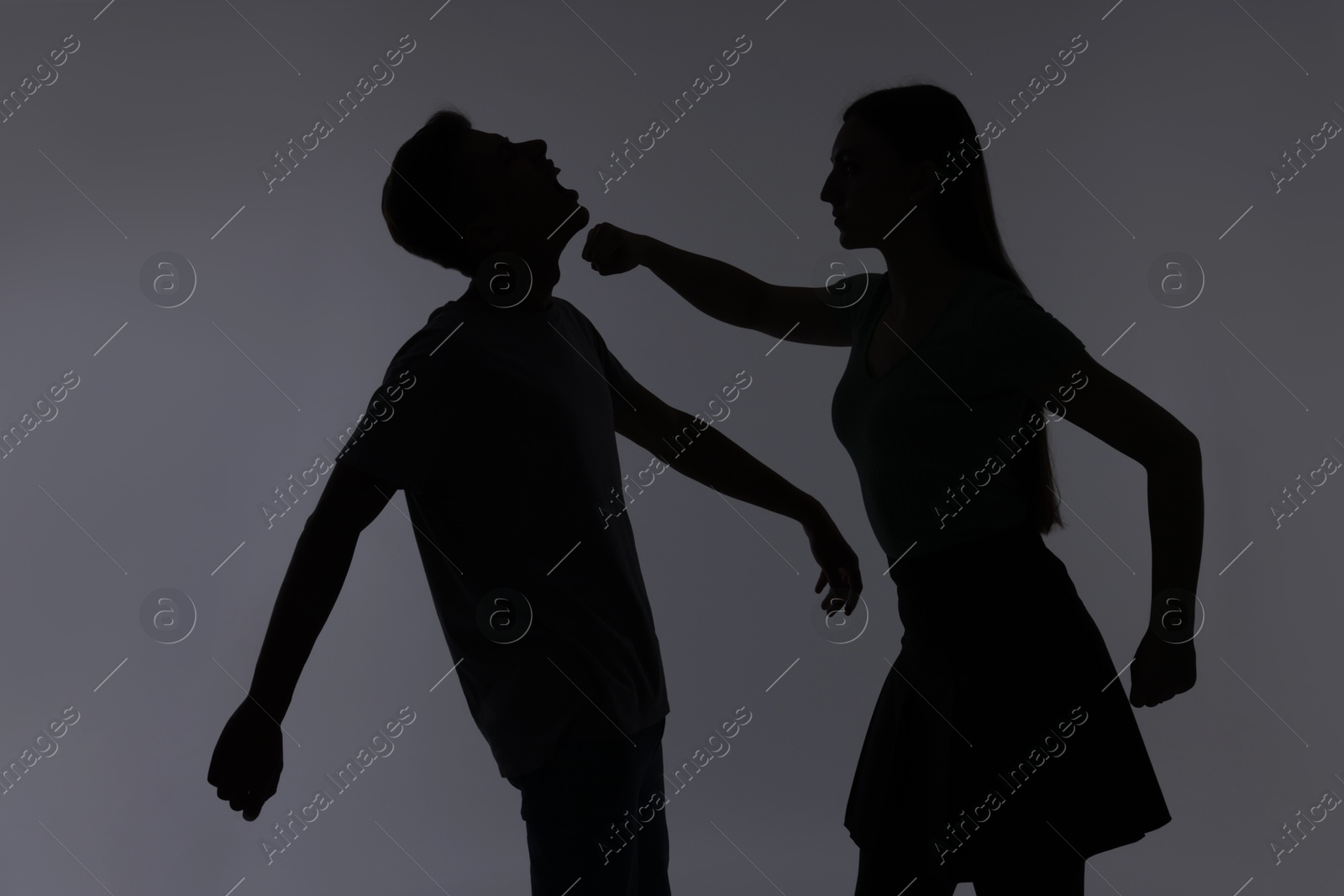 Photo of Domestic violence. Silhouette of woman punching her husband on grey background