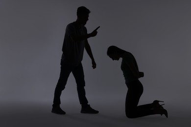 Photo of Domestic violence. Silhouette of man threatening his wife on grey background