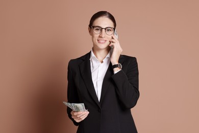 Photo of Banker with dollar banknotes talking on smartphone against brown background