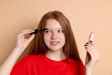 Photo of Smiling teenage girl applying mascara on beige background