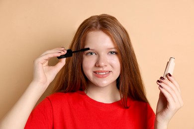 Photo of Smiling teenage girl applying mascara on beige background