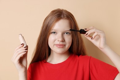 Photo of Teenage girl applying mascara on beige background