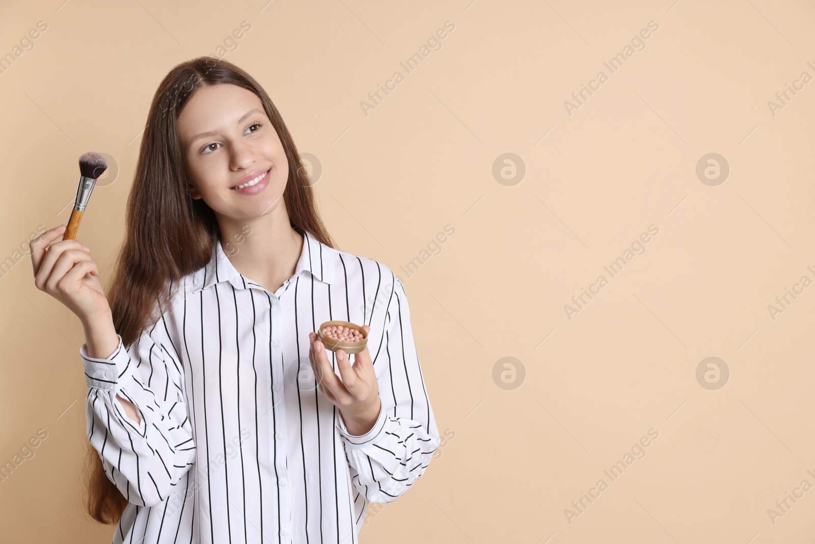 Photo of Smiling teenage girl with blusher and makeup brush on beige background. Space for text