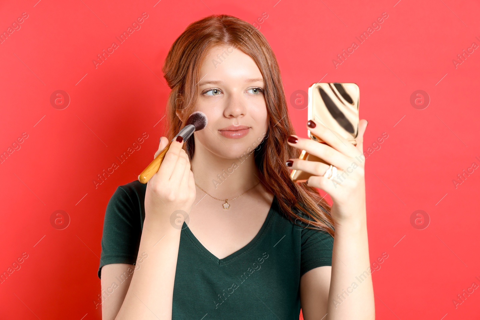 Photo of Teenage girl applying blusher with makeup brush on red background