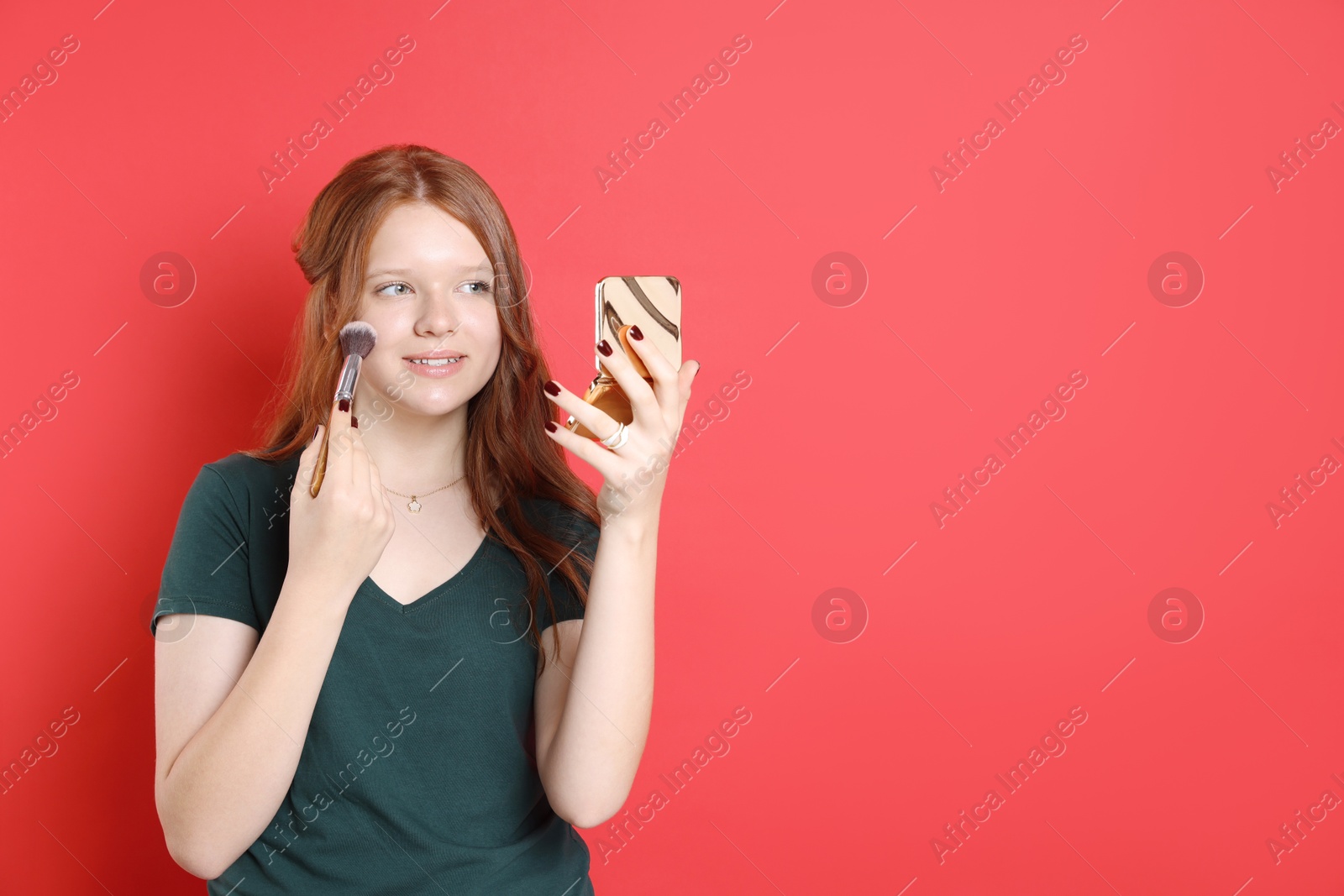 Photo of Smiling teenage girl applying blusher with makeup brush on red background. Space for text