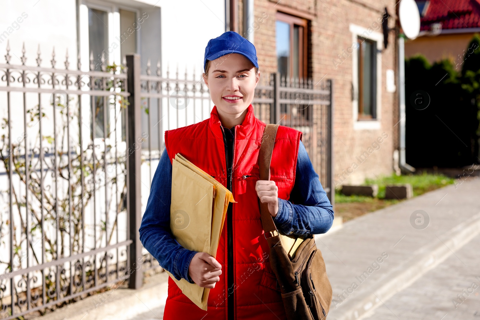 Photo of Mailwoman in uniform with envelopes outdoors. Postal service