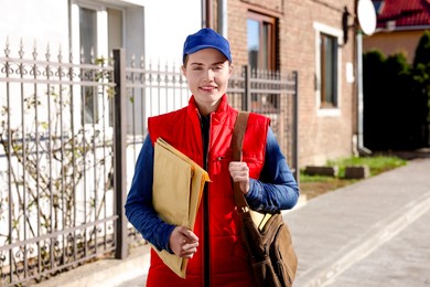 Photo of Mailwoman in uniform with envelopes outdoors. Postal service