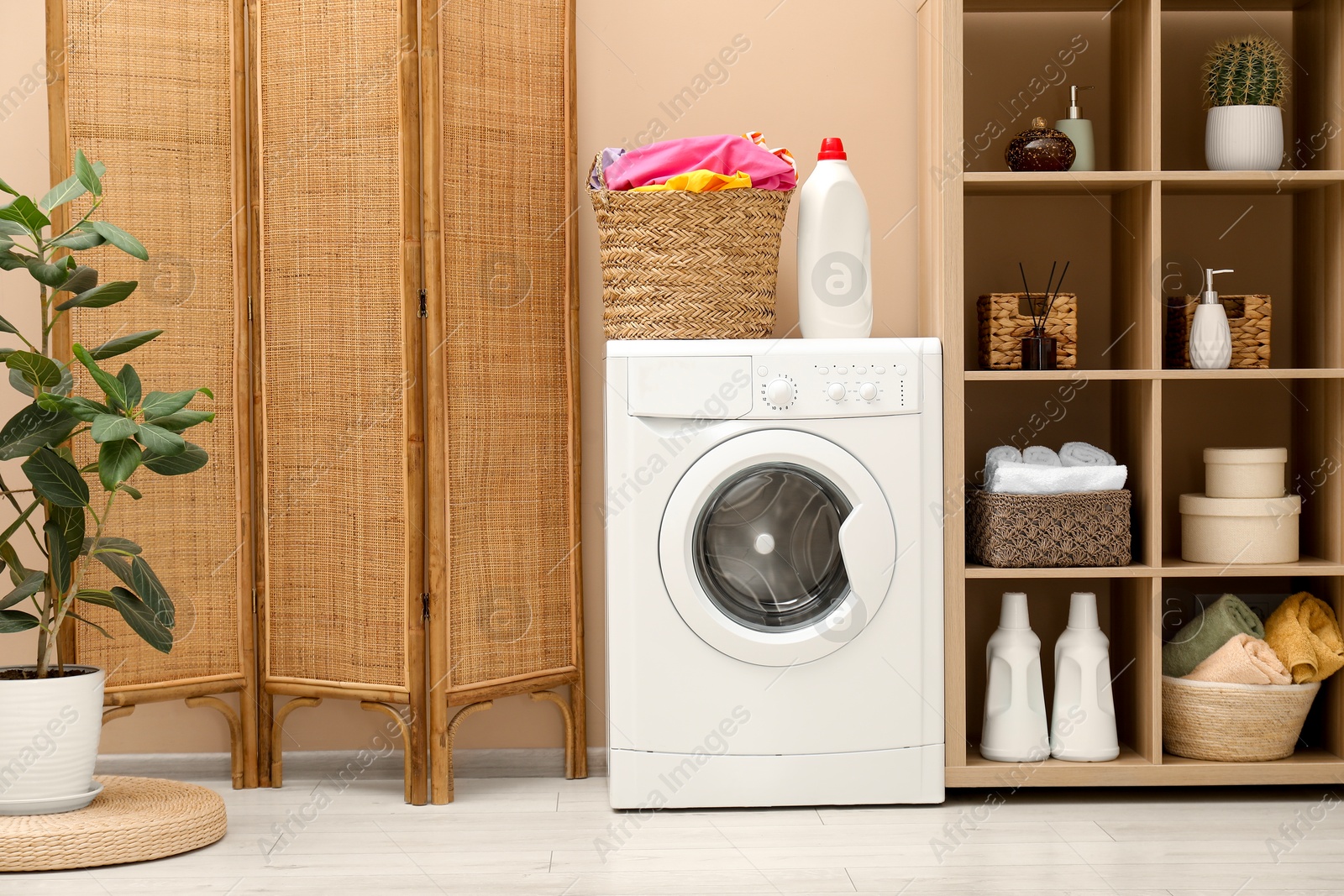 Photo of Wicker basket full of laundry, washing machine and detergent in bathroom