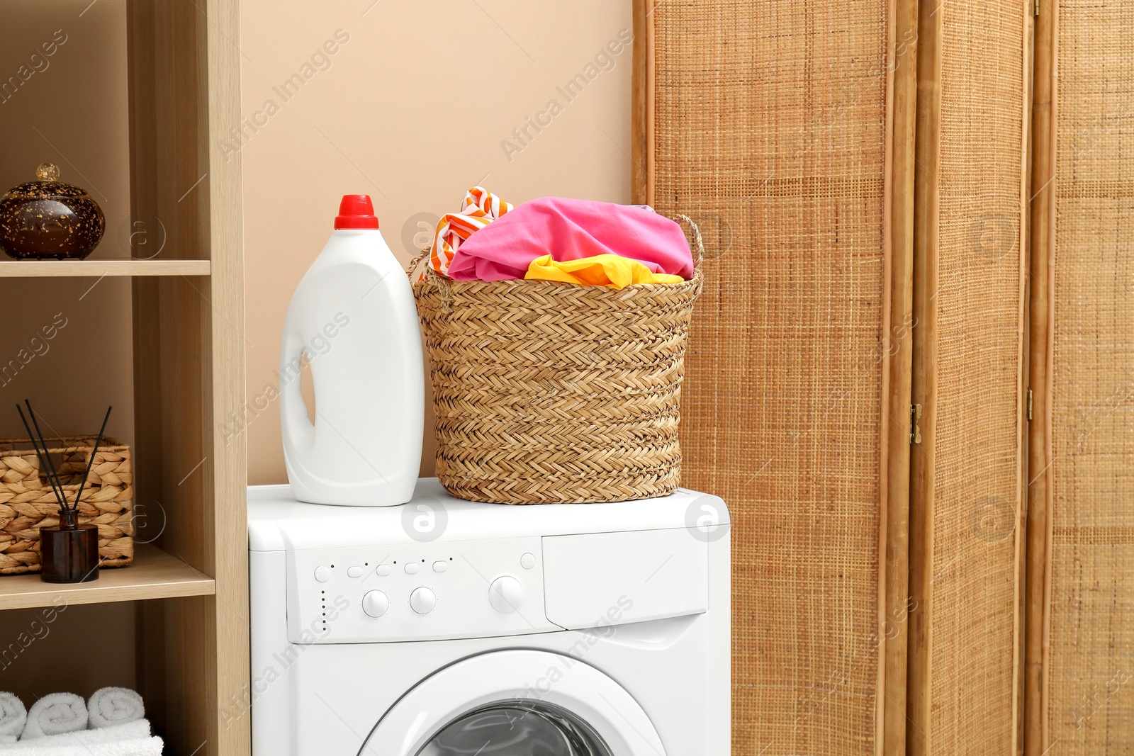 Photo of Wicker basket full of laundry, washing machine and detergent in bathroom