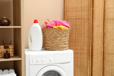 Photo of Wicker basket full of laundry, washing machine and detergent in bathroom