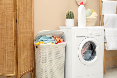 Photo of Wicker basket full of laundry, washing machine and detergent in bathroom