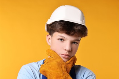 Photo of Teenage boy in hardhat working as builder on orange background