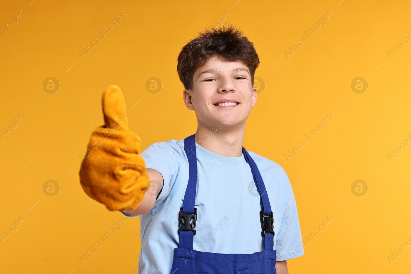 Photo of Teenage boy in protective gloves working as builder on orange background