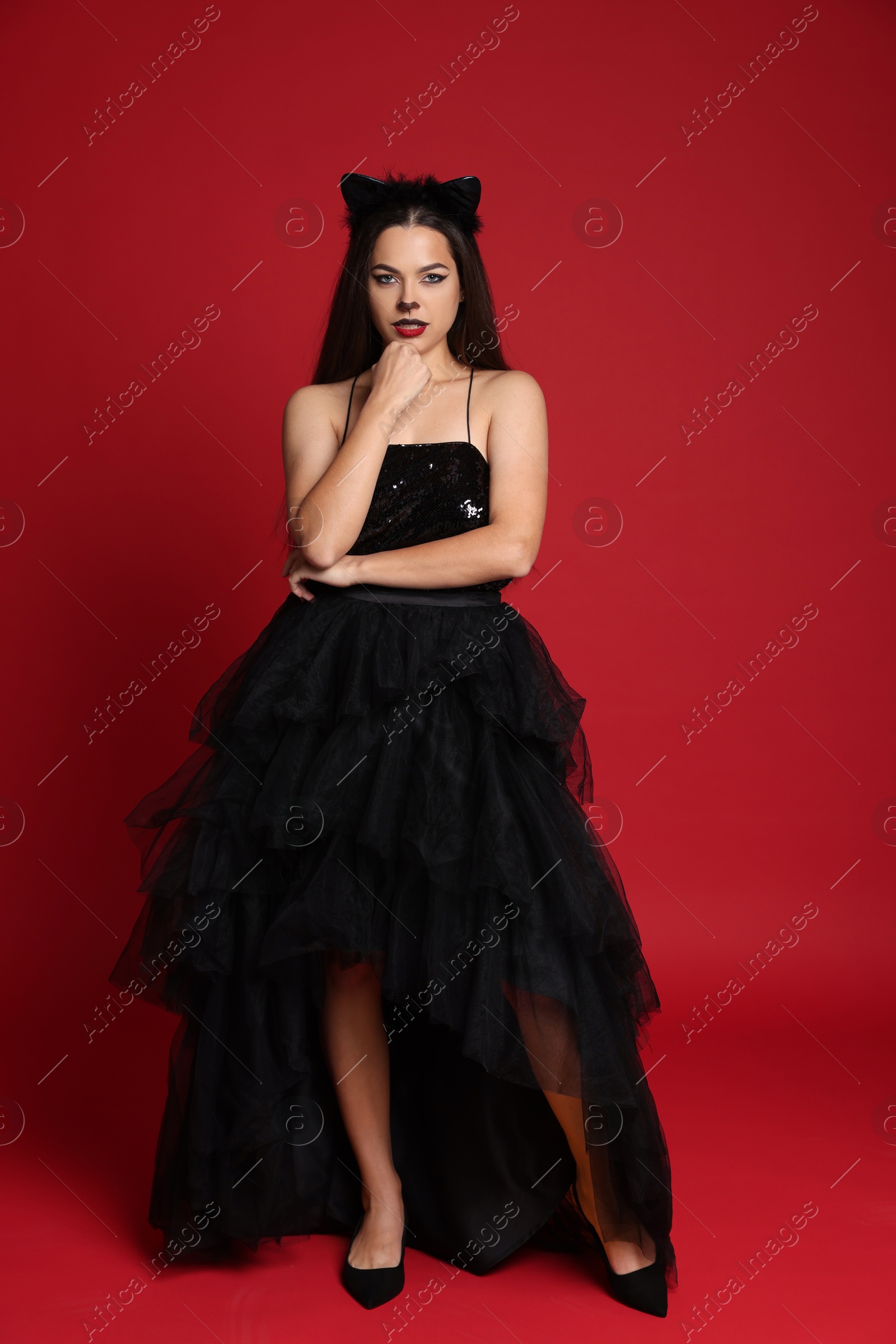 Photo of Woman with cat makeup and ears in beautiful dress on red background