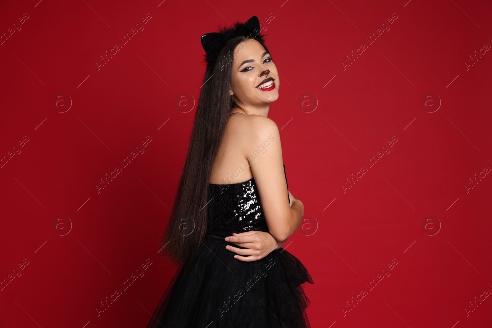 Photo of Woman with cat makeup and ears in beautiful dress on red background