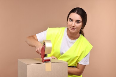 Photo of Girl packing box with adhesive tape on pale brown background. Work for teenagers