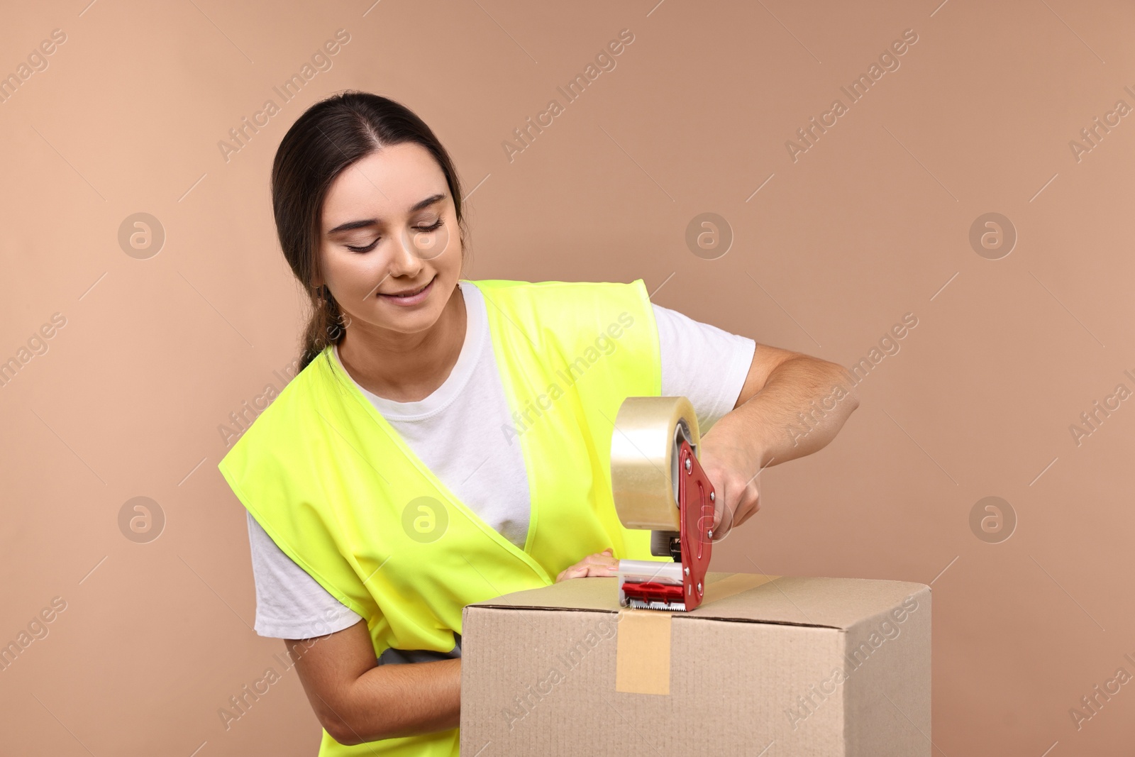 Photo of Girl packing box with adhesive tape on pale brown background. Work for teenagers