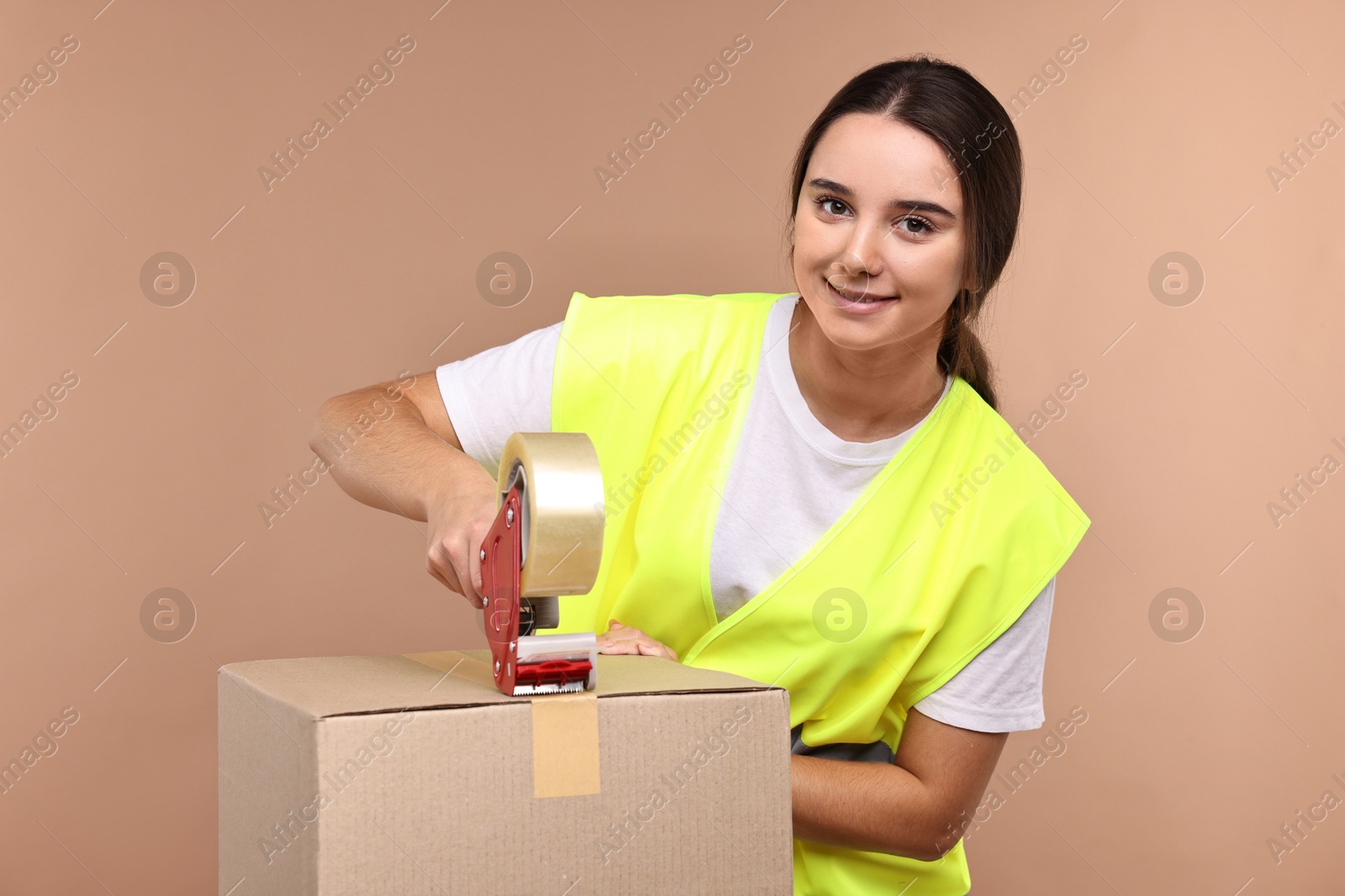 Photo of Girl packing box with adhesive tape on pale brown background. Work for teenagers