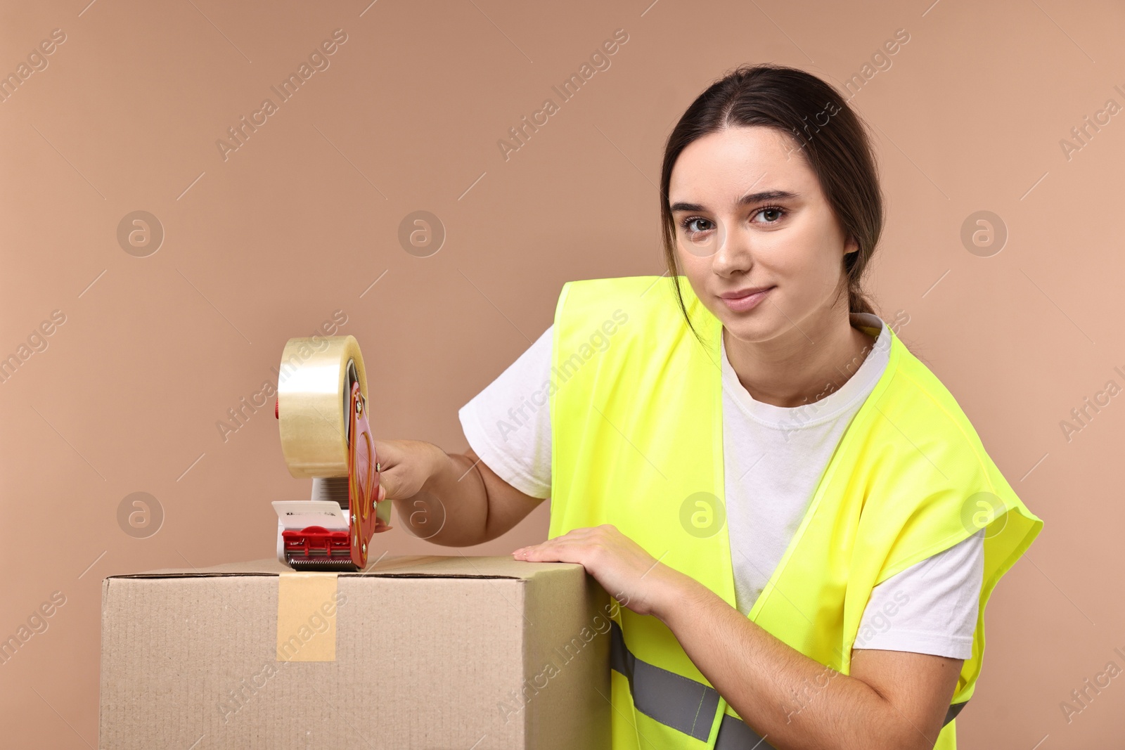 Photo of Girl packing box with adhesive tape on pale brown background. Work for teenagers