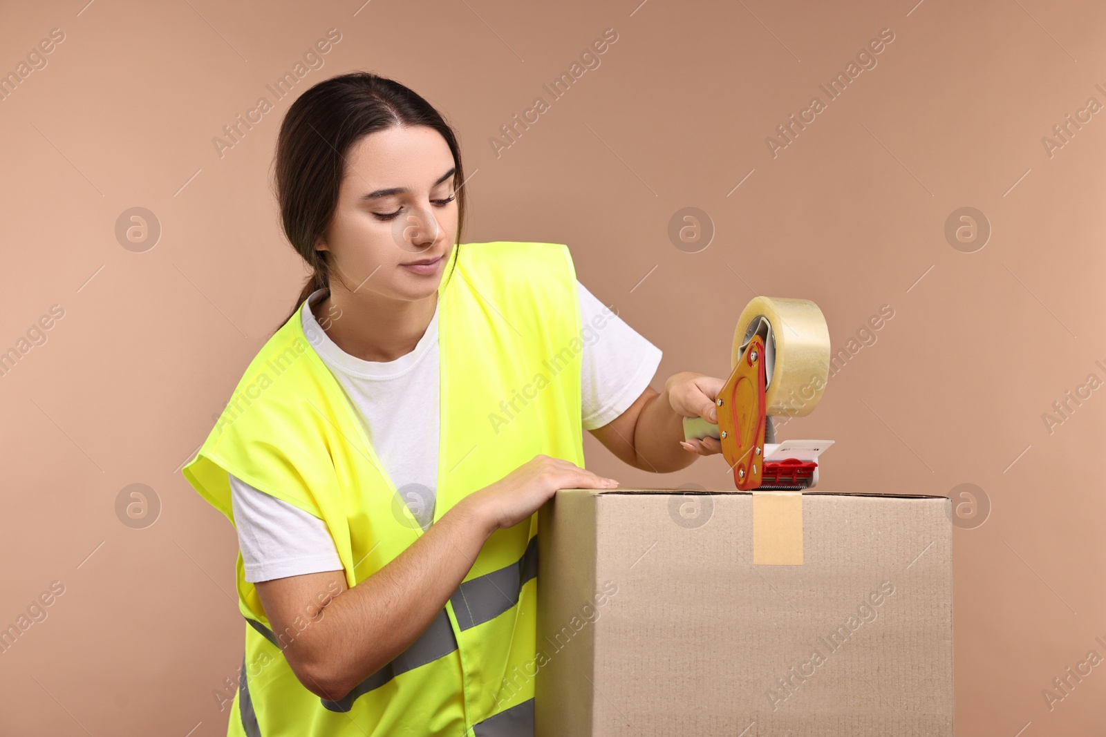 Photo of Girl packing box with adhesive tape on pale brown background. Work for teenagers