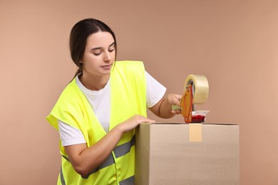 Photo of Girl packing box with adhesive tape on pale brown background. Work for teenagers