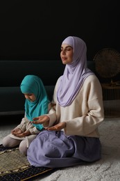 Muslim woman and her daughter praying on mat at home