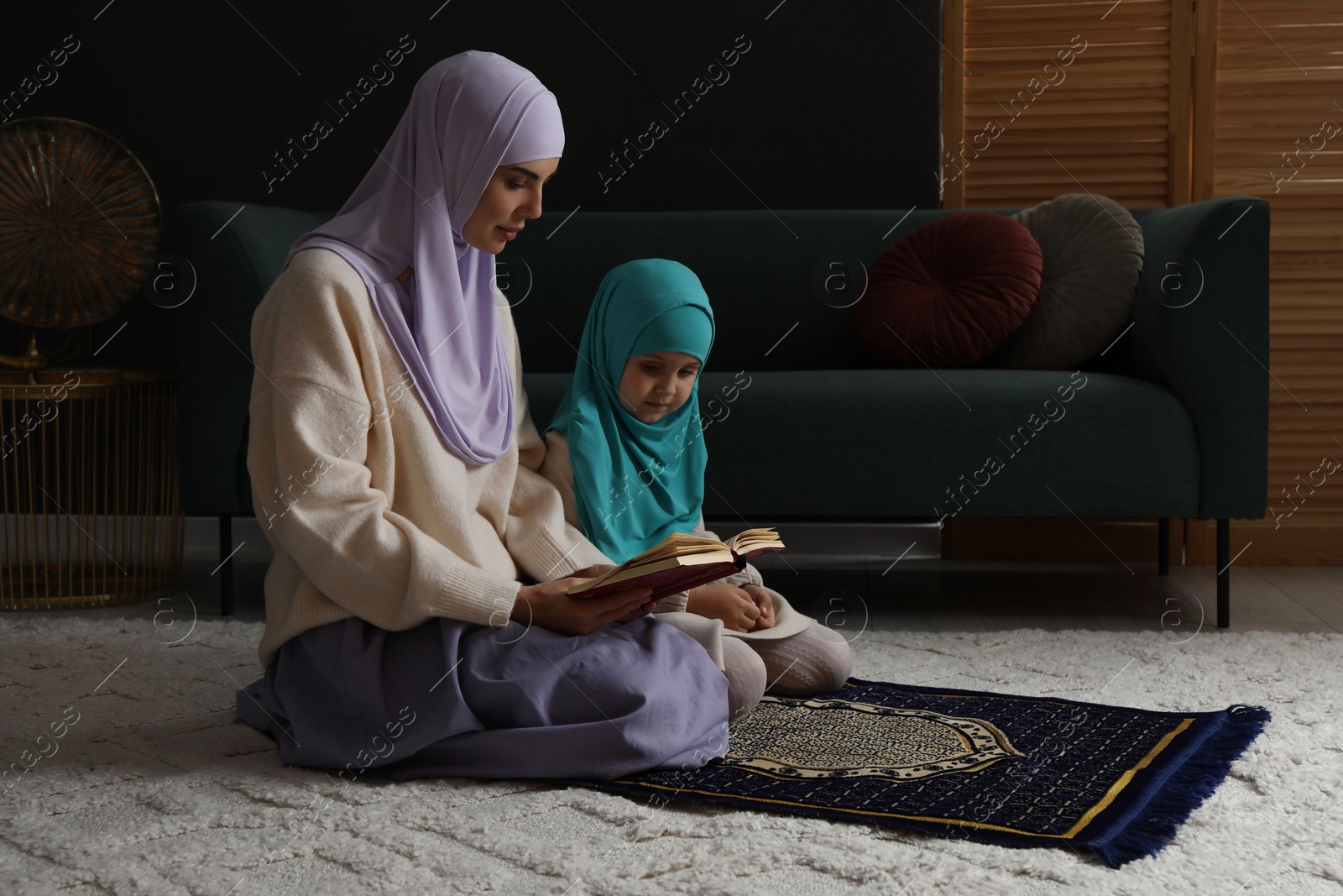 Photo of Muslim woman and her daughter with Quran praying on mat at home