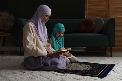 Photo of Muslim woman and her daughter with Quran praying on mat at home