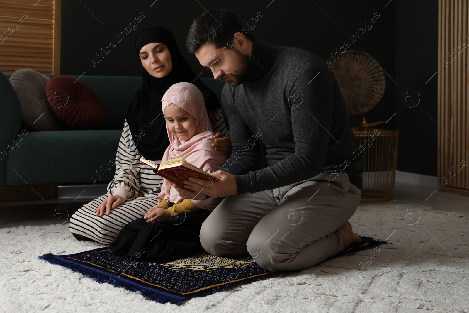 Photo of Muslim family with Quran praying on mat at home