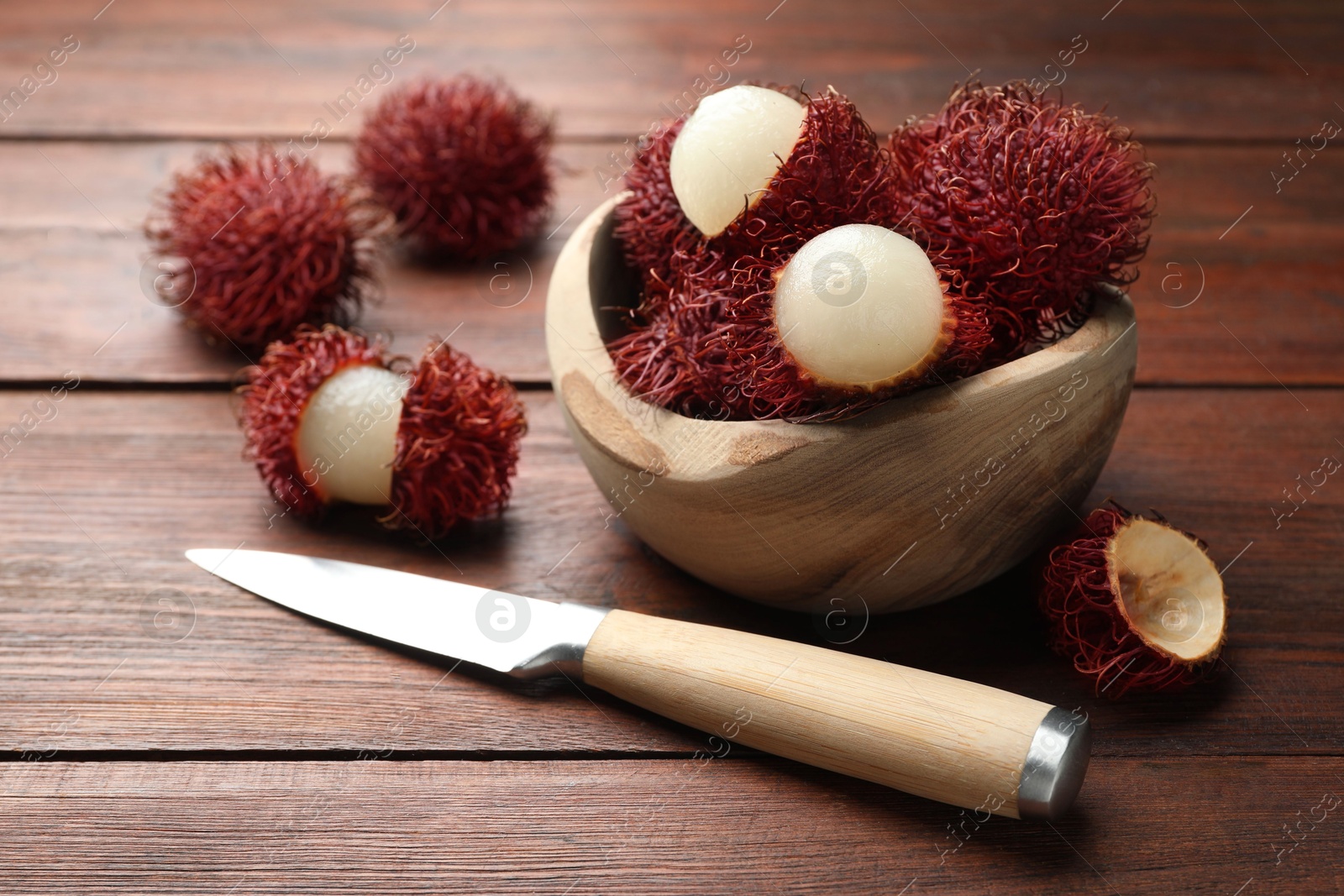 Photo of Delicious ripe rambutans in bowl and knife on wooden table