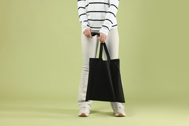 Photo of Woman with blank black shopper bag on color background, closeup. Mockup for design