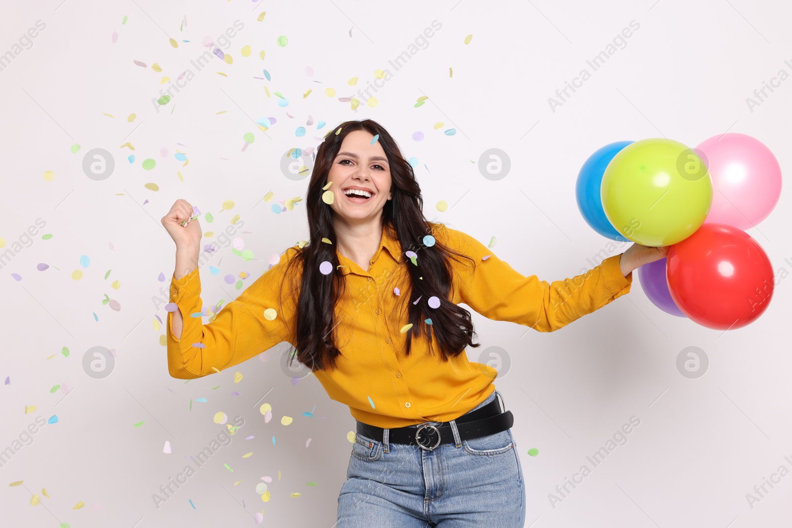 Photo of Happy woman with colorful balloons under falling confetti on white background. Surprise party