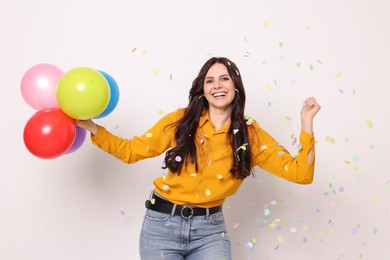 Photo of Happy woman with colorful balloons under falling confetti on white background. Surprise party