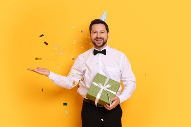 Photo of Happy man with gift box under falling confetti on orange background. Surprise party