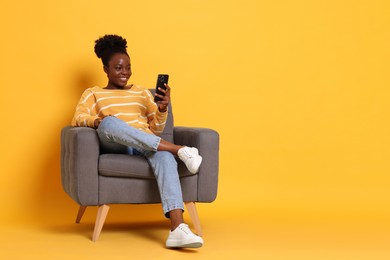 Photo of Smiling woman with smartphone sitting in armchair on yellow background. Space for text