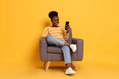 Photo of Smiling woman with smartphone sitting in armchair on yellow background