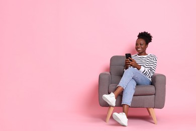 Photo of Smiling woman with smartphone sitting in armchair on pink background. Space for text