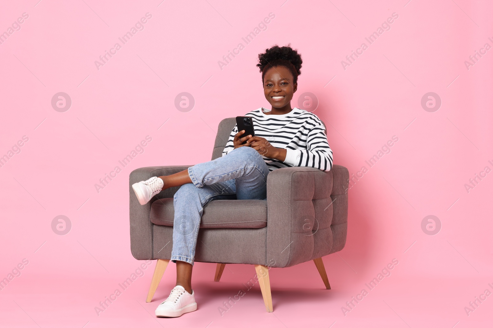 Photo of Smiling woman with smartphone sitting in armchair on pink background