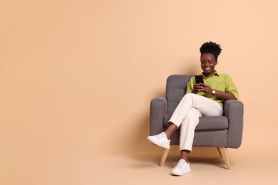 Photo of Smiling woman with smartphone sitting in armchair on beige background. Space for text