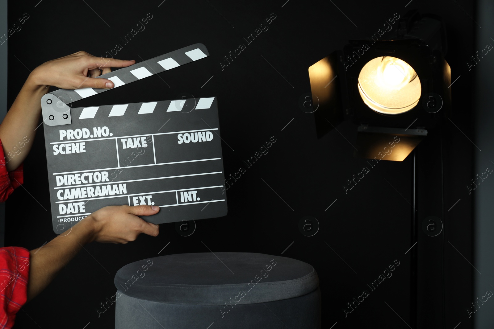 Photo of Woman with clapperboard near spotlight on black background, closeup