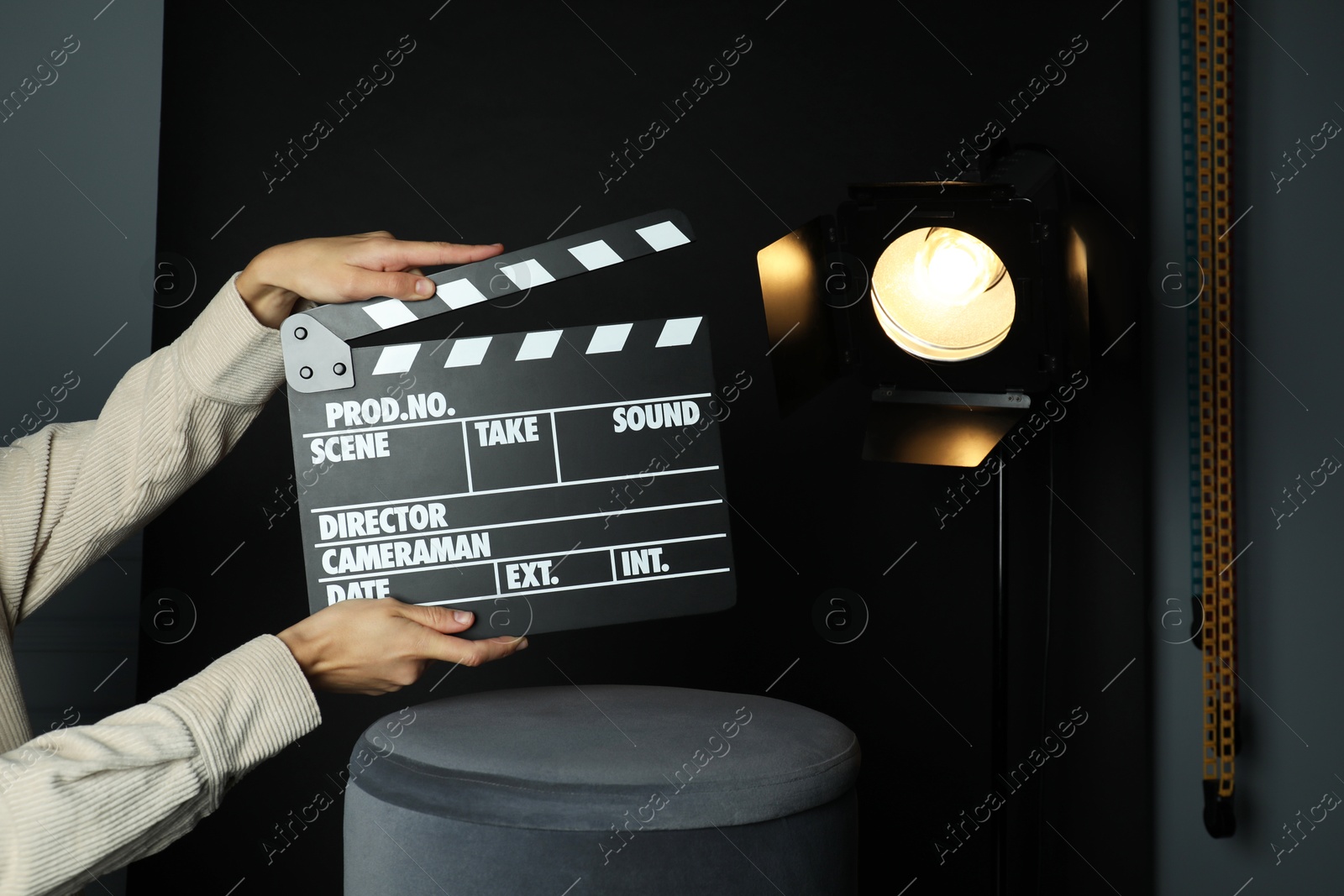 Photo of Woman with clapperboard near spotlight on black background, closeup